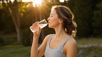 une femme buvant un verre d'eau sous le soleil couchant à la lisière d'une forêt