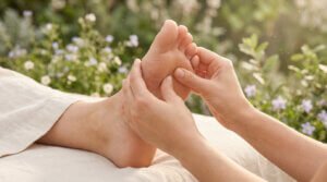 Détail d'une séance de réflexologie plantaire en extérieur. Les mains d'un thérapeute massent le pied, apportant un soulagement pour les allergies.