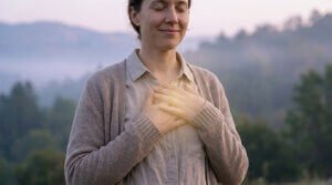 Une femme souriante, yeux clos, les mains croisées sur la poitrine, une lueur douce émane, sur fond de nature sereine.